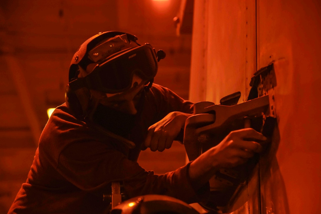 A sailor illuminated by red light cleans the wing of an aircraft.