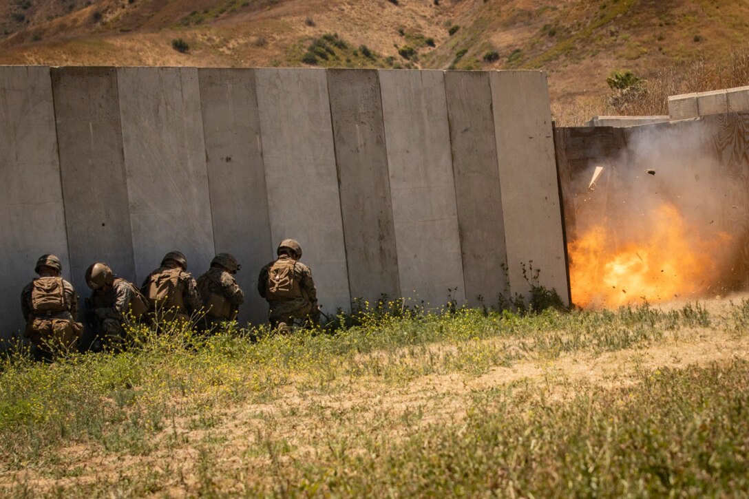 Marines crouch next to a wall during a small explosion.