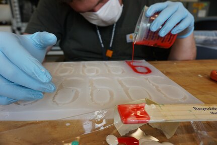 Josh Duck, a mechanical engineer in the Additive Manufacturing Project Office at Naval Surface Warfare Center Carderock Division, pours urethane into a mold to make a new set of door handles.