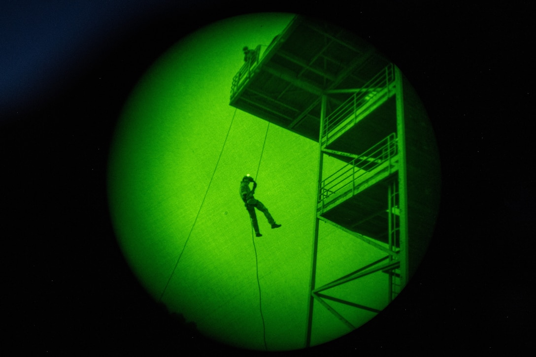 A sailor rappels down a rope illuminated by a green light.