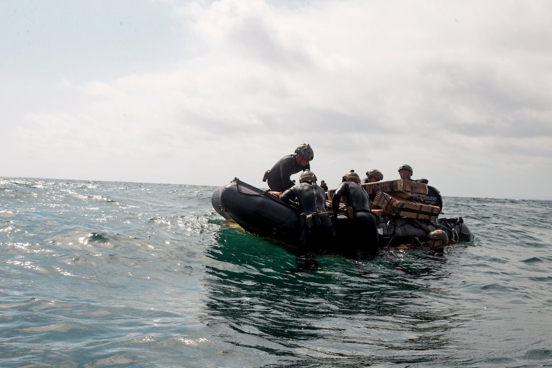 Marines in wet suits sit or swim around a rubber boat.