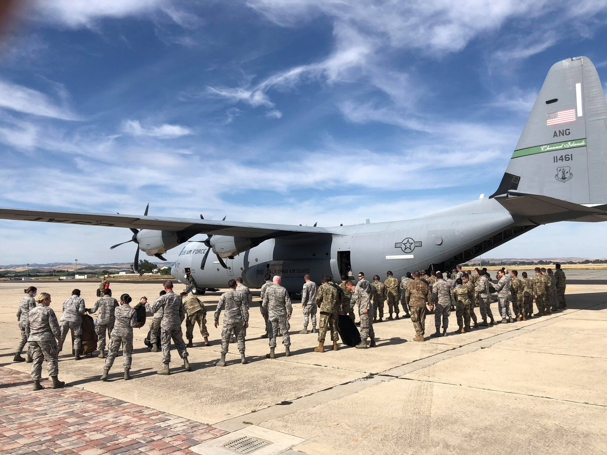 A photograph of multiple California Air National Guard airmen waiting to board  a C-130J Super Hercules military aircraft at the Paso Robles Municipal airport.