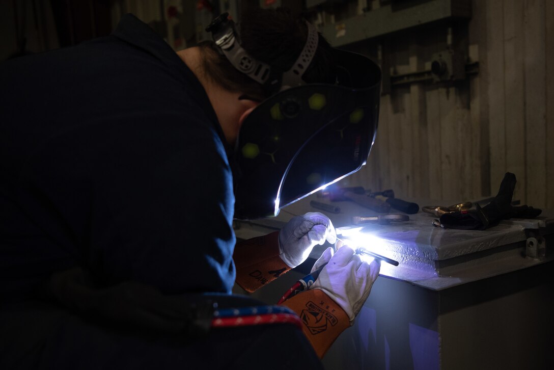 A man wearing protective gear welds an object.