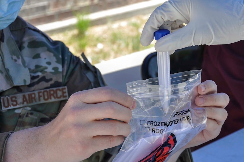 An airman holds a biohazard bag open for a soldier who collected a nasal swab sample from a local resident.