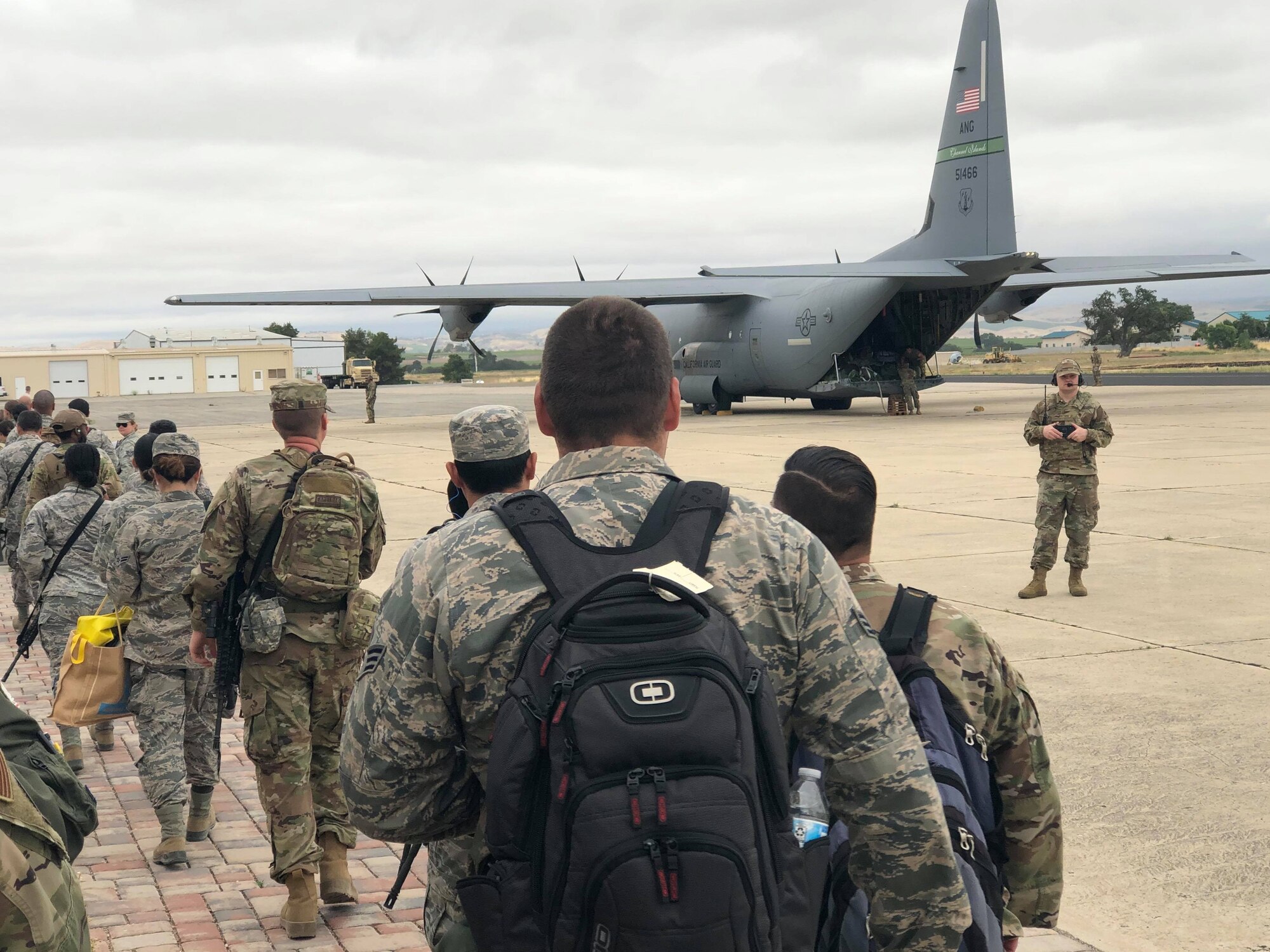 A photograph of multiple California Air National Guard airmen waiting to board  a C-130J Super Hercules military aircraft at the Paso Robles Municipal airport.