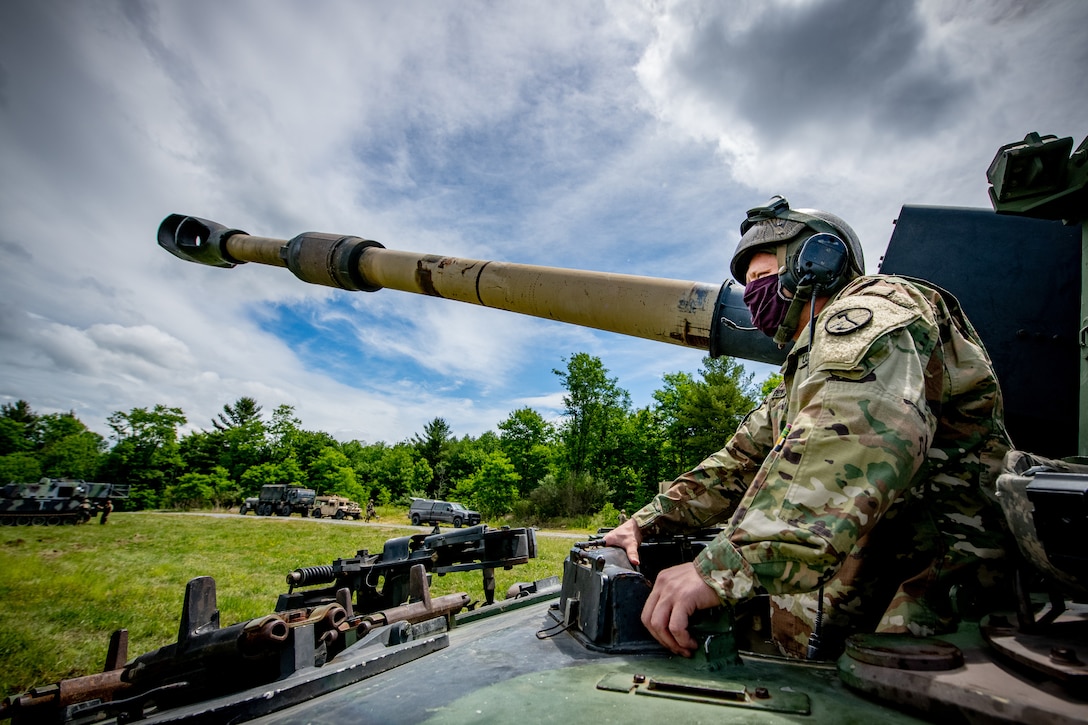 A soldier stands next to large gun and looks out over a field.