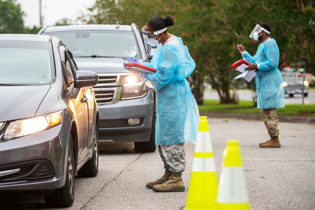 Several guardsmen wearing personal protective equipment take information from passengers in their cars at a drive-through testing site.