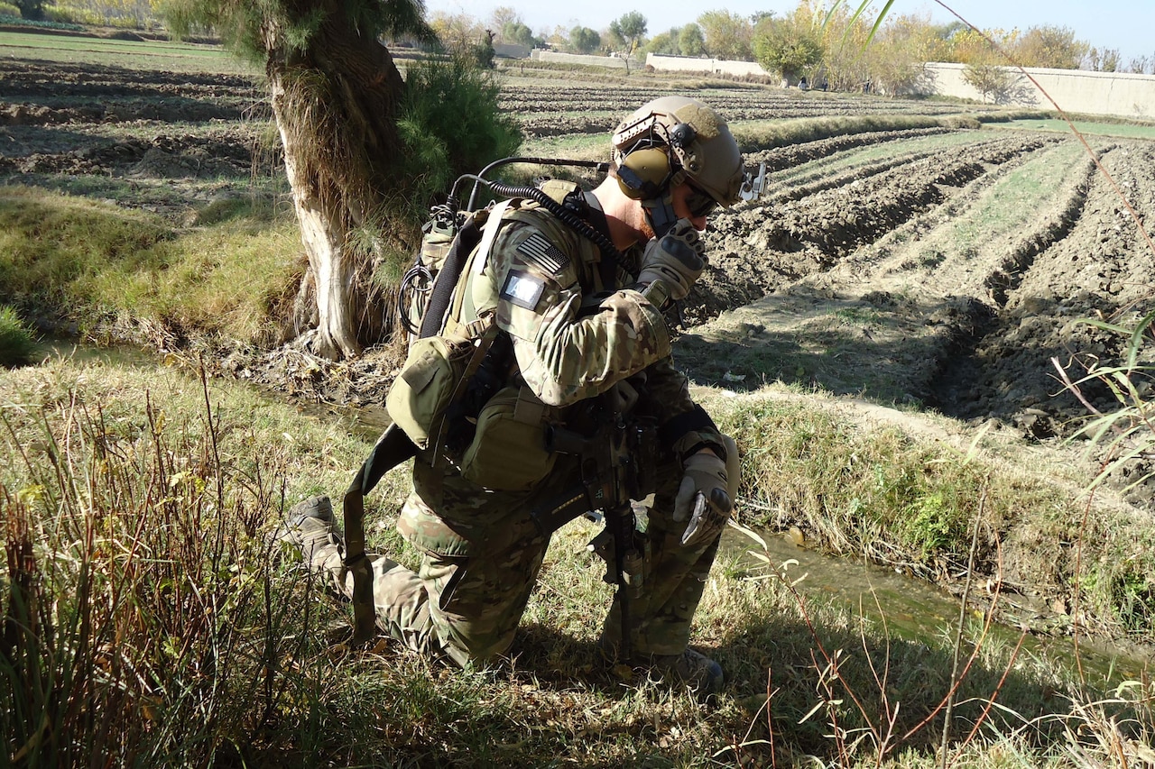 A soldier is down on one knee in a field.