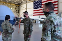 An Airman briefs two commanders in front of an MQ-9 Reaper nose and United States flag.