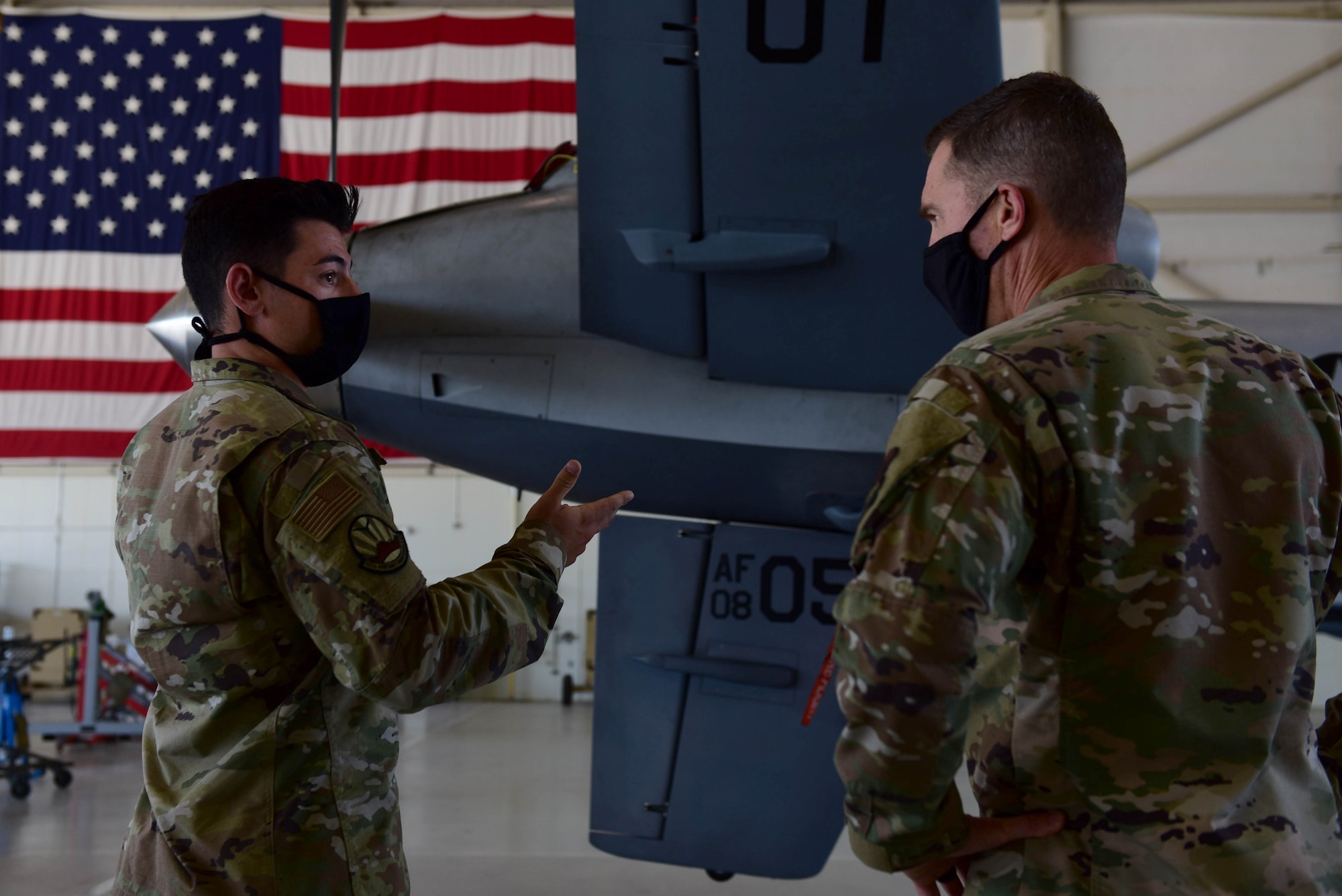 A Airman briefs a commander in front of an MQ-9 Reaper tail and United States flag.