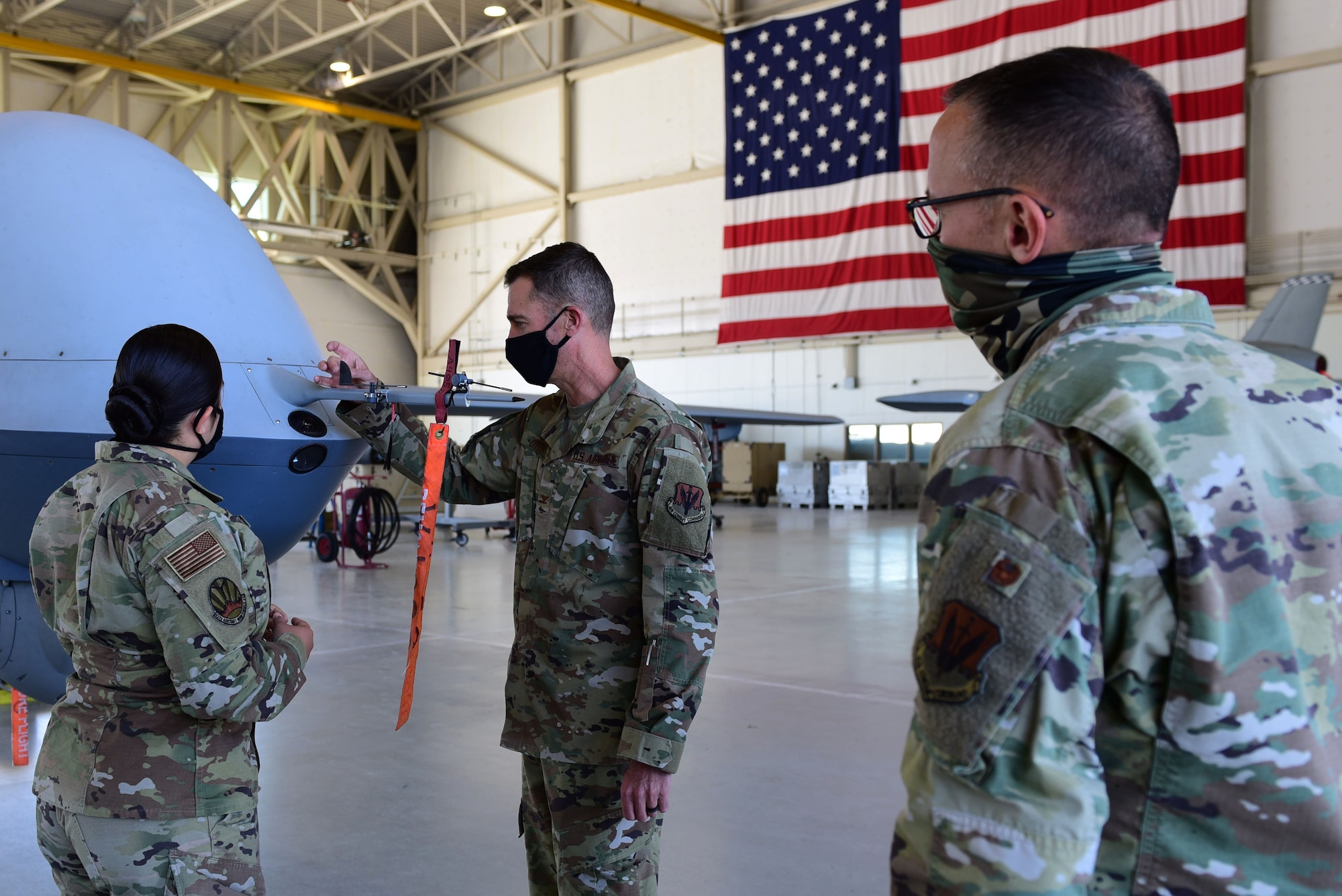 An Airman briefs two commanders in front of an MQ-9 Reaper nose and United States flag.