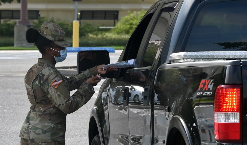 A soldier wearing a face mask assists a motorist at at COVID-19 test site.