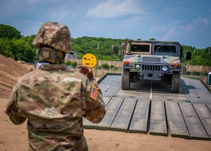 A Soldier assigned to the Connecticut National Guard's 250th Multi-Role Bridge Company guides a Humvee across a dry support bridge the unit constructed while training at Stones Ranch Military Reservation June 10, 2020. The bridge enables military units to cross gaps in terrains up to nearly 151 feet wide.