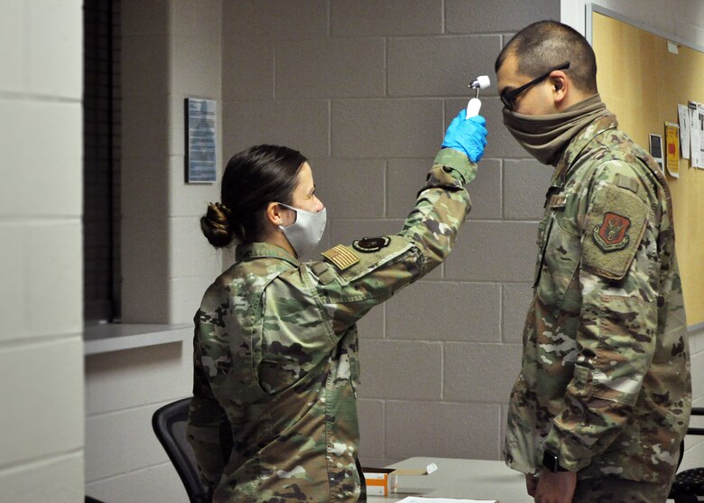 Senior Airman Chloe Van Hoose, 445th Force Support Squadron career development specialist, checks the temperature of Master Sgt. Bryan Ulloa, 445th FSS services craftsman, as he enters the building, June 6, 2020.  This safety measure is taken in response to the COVID-19 pandemic. (U.S. Air Force photo/Senior Airman Angela Jackson)