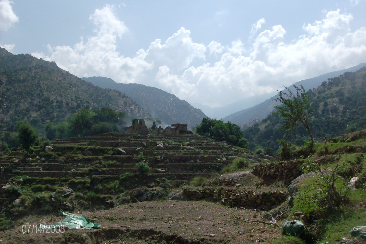 Dilapidated rock buildings sit atop a hillside in between mountains.