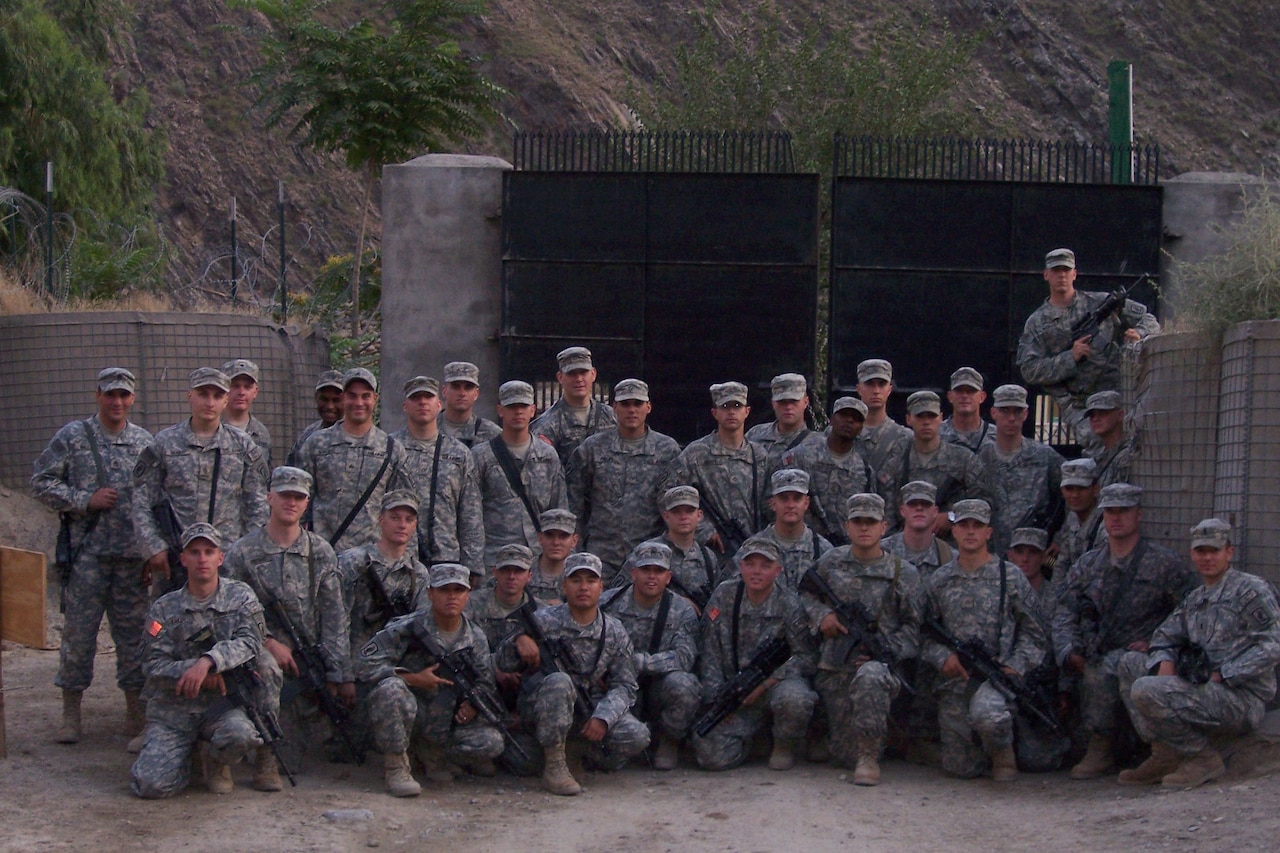 A platoon of soldiers pose near a gate in the desert.