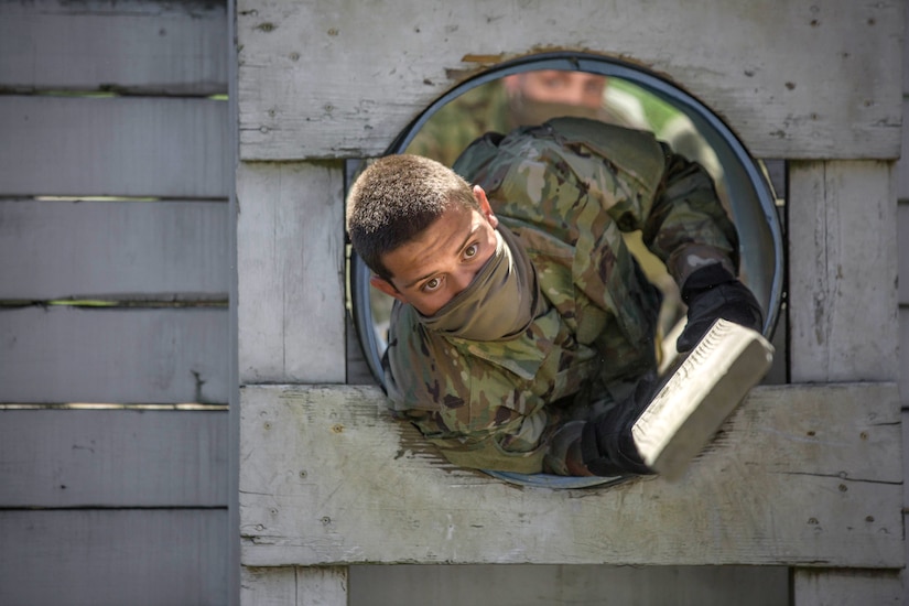 A service member crawls through a tube carrying a board.