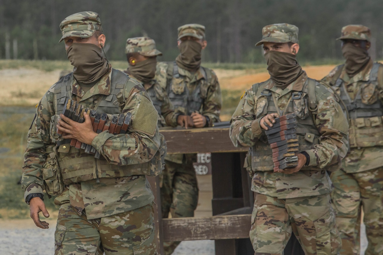 Service members in uniform and wearing face masks carry ammunition magazines.