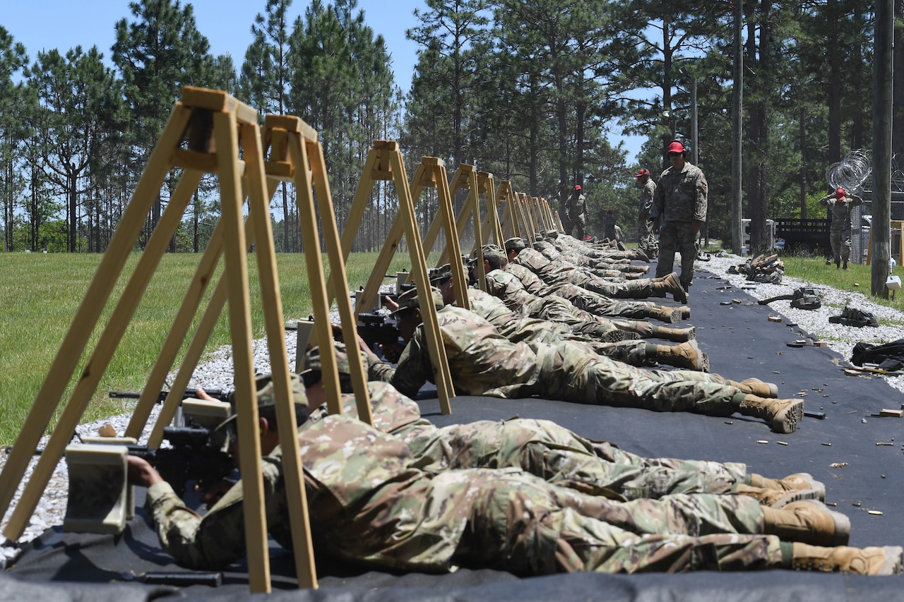 Service members lay on the ground and aim their rifles downrange.