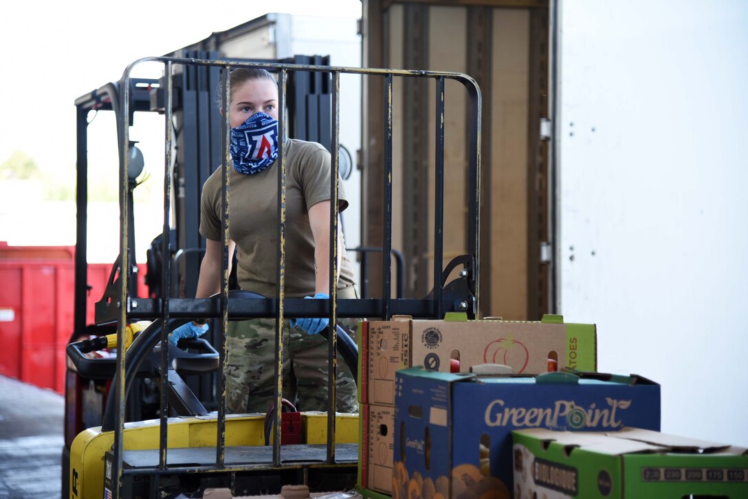 A service member wearing a mask drives a forklift.