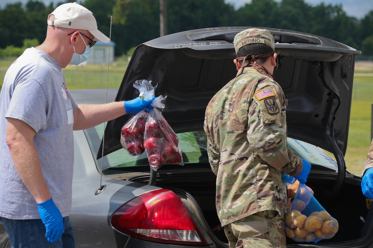 A soldier and a civilian place bags of food into a vehicle.
