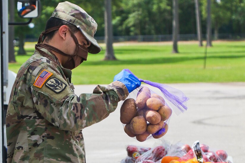 A soldier wearing a face mask sorts produce for distribution.