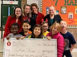 Four women and six school children pose with a check presented to Coles Elementary School in Manassas, Va., Dec. 20, 2019.