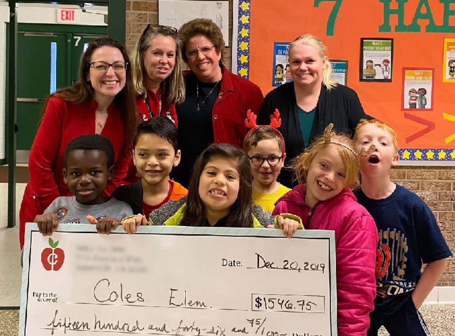 Four women and six school children pose with a check presented to Coles Elementary School in Manassas, Va., Dec. 20, 2019.