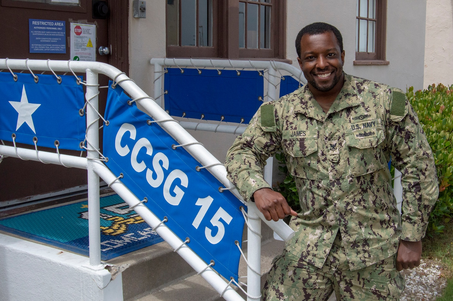 Intelligence Specialist 2nd Class Joshua James, from Savannah, Ga., stands in front of the entrance of Commander, Carrier Strike Group (CCSG) 15. CCSG-15 conducts integrated training to provide Fleet Commanders with deployable combat ready maritime forces in support of global operations. (U.S. Navy photo by Mass Communication Specialist 1st Class Christopher Cavagnaro/Released)
