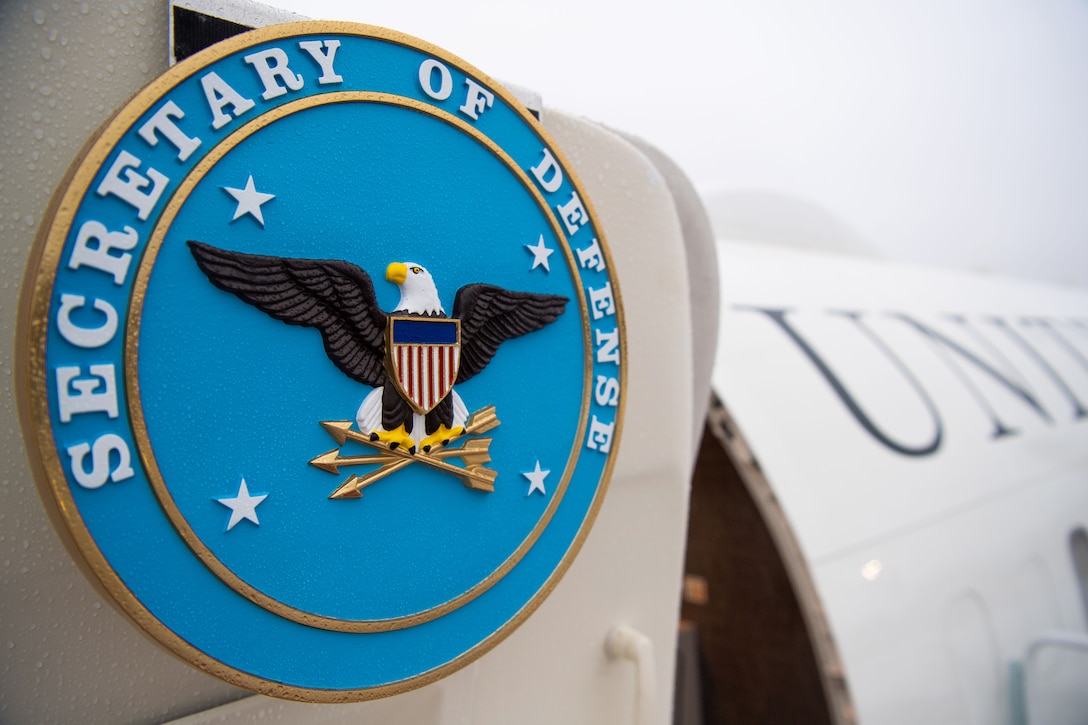 The defense secretary's seal is displayed on an open aircraft door.