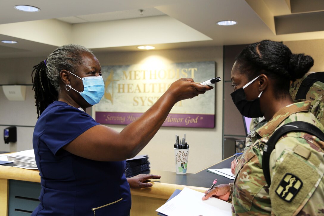 A nurse wearing a mask takes the temperature of a service member wearing a mask.