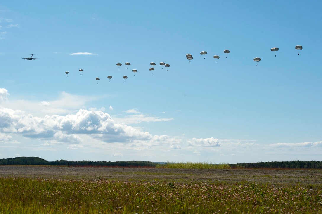 Paratroopers jump from military aircraft over a grassy field.