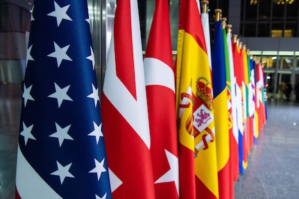 A row of flags stand in a lobby-like room.