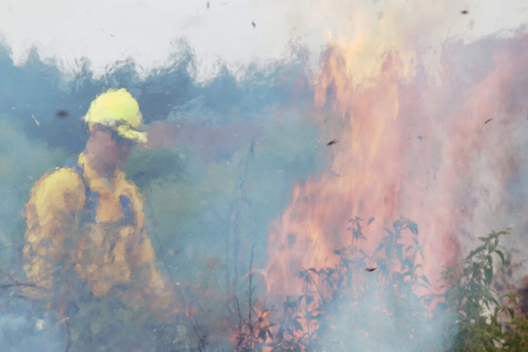 A man in firefighting gear stands next to a large fire.