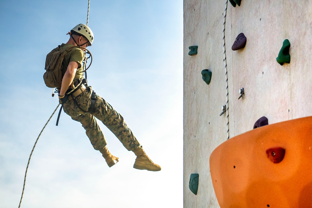 A Marine rappels down a rocking climbing wall.
