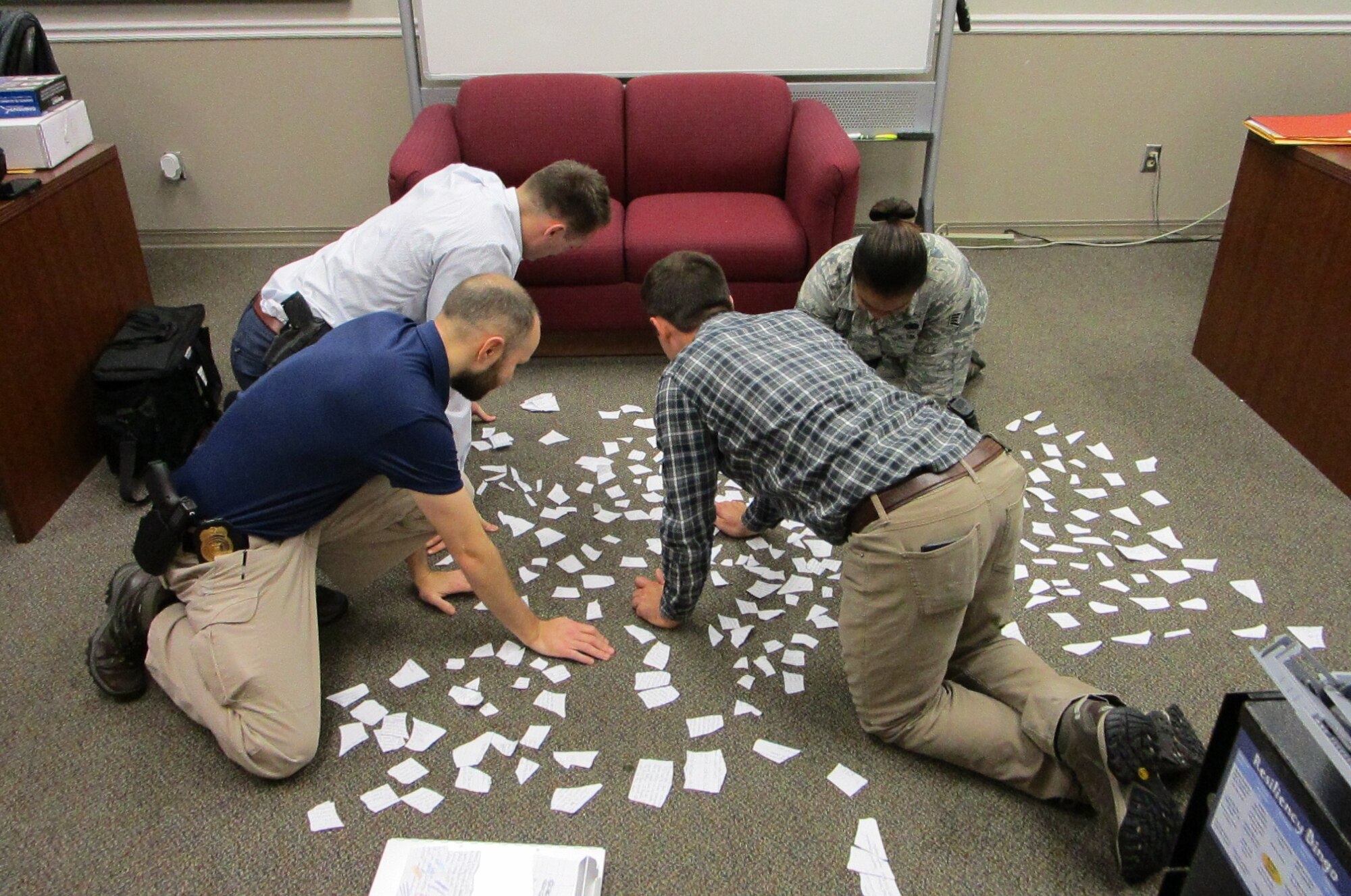 Special Agent Hunter Young, front left, and others re-assemble ripped papers retrieved from the apartment of a deceased person. Gloves were not used since the letter was retrieved days after the incident via the Summary Court Officer and it was clear it was not a suicide note. The note was used to identify witnesses. (Courtesy photo)