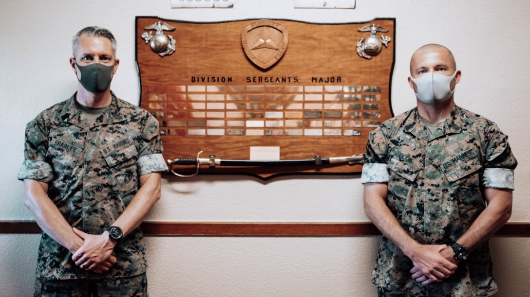 U.S. Marine Corps Sgt. Maj. Dennis M. Bradley (left) and Sgt. Maj. Eric D. Cook stand in front of the “Division Sergeants Major” board in the 3rd Marine Division Headquarters building on Camp Courtney, Okinawa, Japan, July 13, 2020. This traditional board captures the lineage of the senior enlisted leaders who have carried the title of Division Sergeant Major. Bradley will transfer the title to Sgt. Maj. Cook on July 15 without a ceremony to avoid formations or large gatherings, therefore lowering the chances to spread COVID-19. (U.S. Marine Corps photo by Cpl. Josue Marquez)