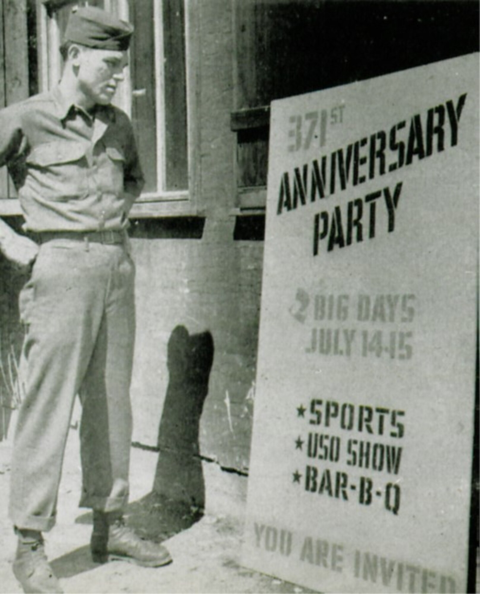 The 371st Fighter Group celebrated its second anniversary in Germany in July, 1945.  Here a unit member looks on to an advertisement for the festivities.   (The Story of the 371st Fighter Group in the E.T.O.)