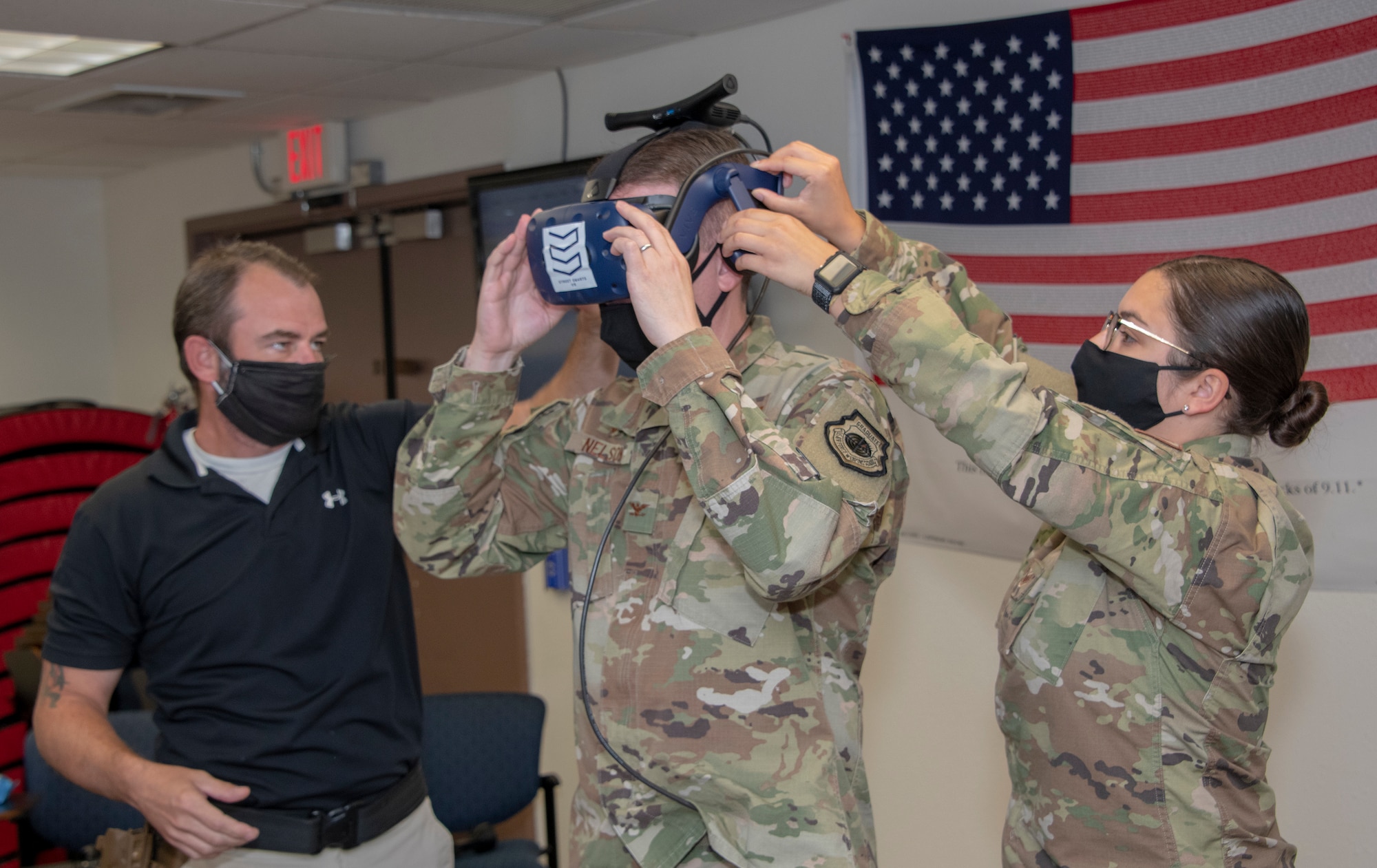 Brandon Feldmann, left, 60th Security Forces Squadron training instructor, and U.S. Air Force Staff Sgt. Deanna Ciesiel, right, 60th SFS training instructor, assist Col. Jeffrey Nelson, 60th Air Mobility Wing commander, don a virtual reality visor during Leadership Rounds July 10, 2020, at Travis Air Force Base, California. The 60th SFS uses this system to train and evaluate Airmen on use-of-force law enforcement technique.  The Leadership Rounds program provides 60th AMW leadership an opportunity to interact with Airmen and get a detailed view of each mission performed at Travis AFB. (U.S. Air Force photo by Heide Couch)