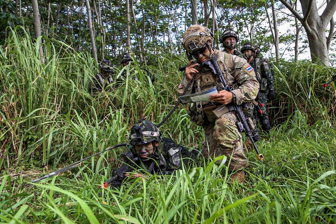 Soldiers crouch in a grassy area.