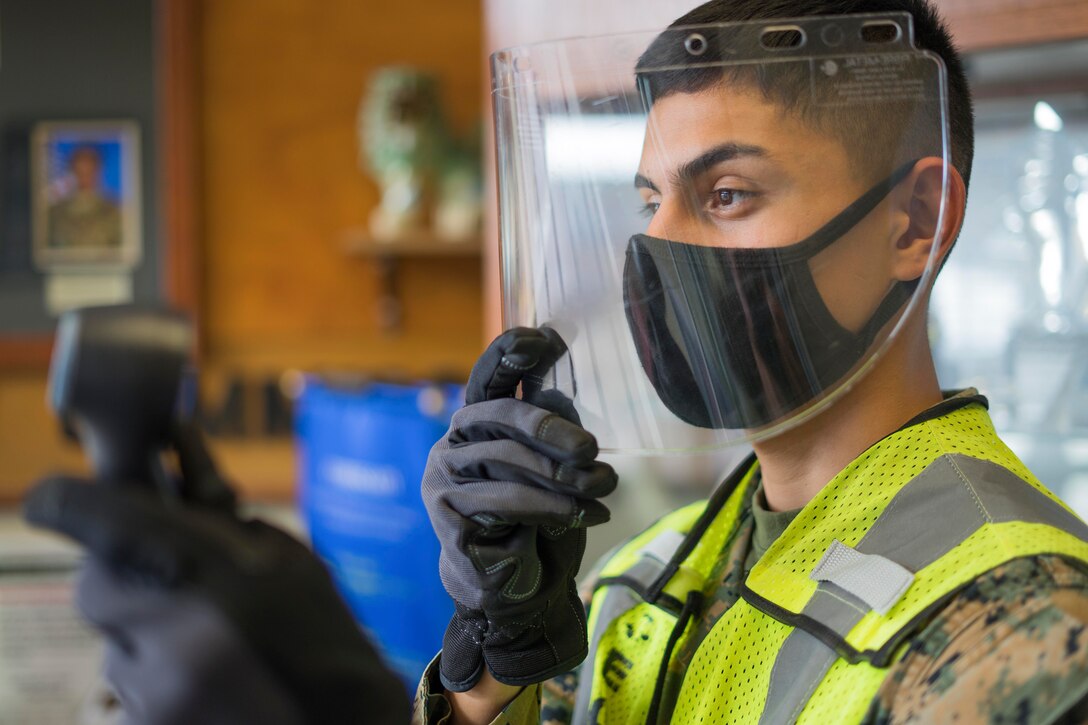 A Marine wearing personal protective equipment holding a thermometer.