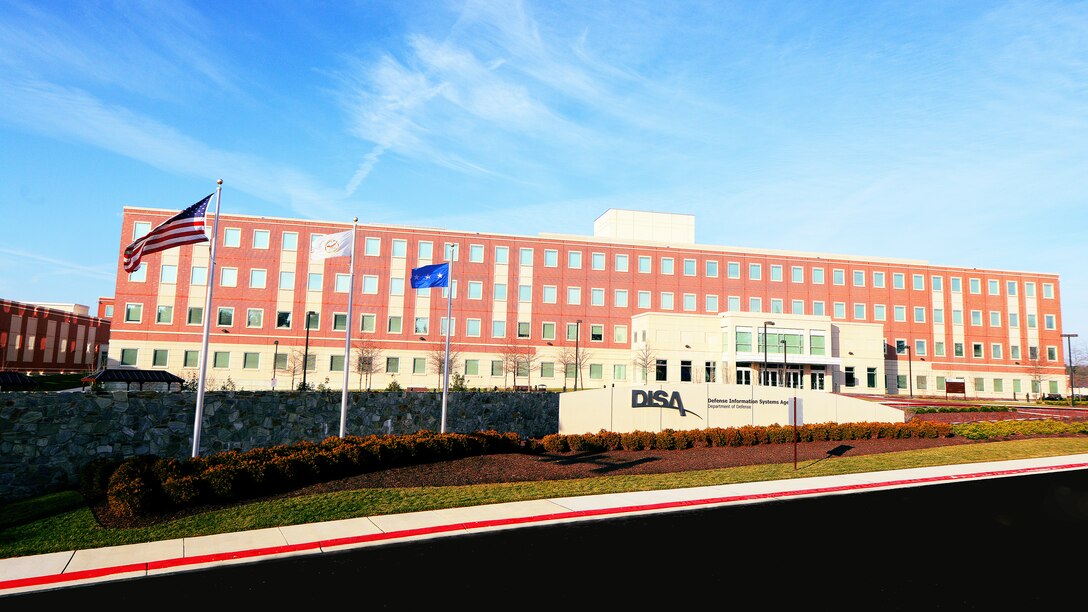 A brick building sits under a blue sky. In front, a wall is inscribed with “DISA” and “Defense Information Systems Agency.”