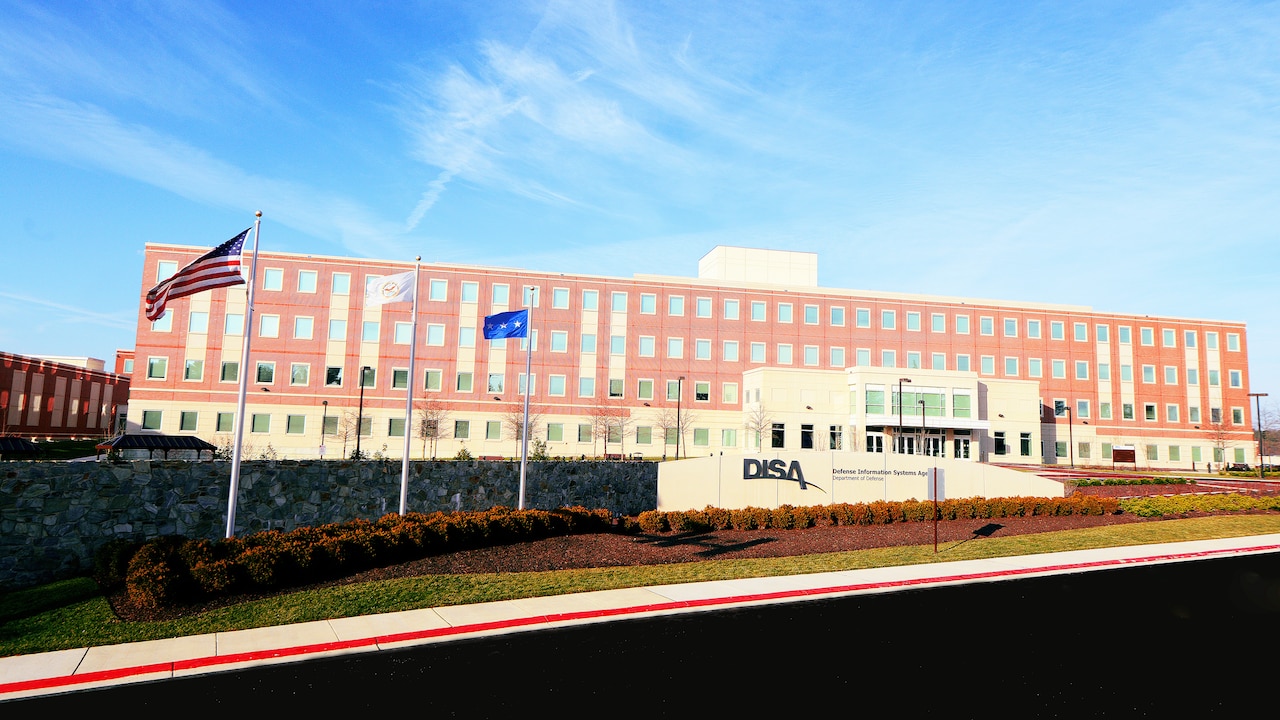 A brick building sits under a blue sky. In front, a wall is inscribed with “DISA” and “Defense Information Systems Agency.”