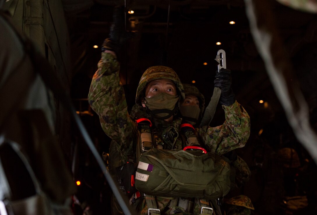 A Japan Ground Self Defense Force paratrooper hooks his parachute to a static line aboard a C-130J Super Hercules