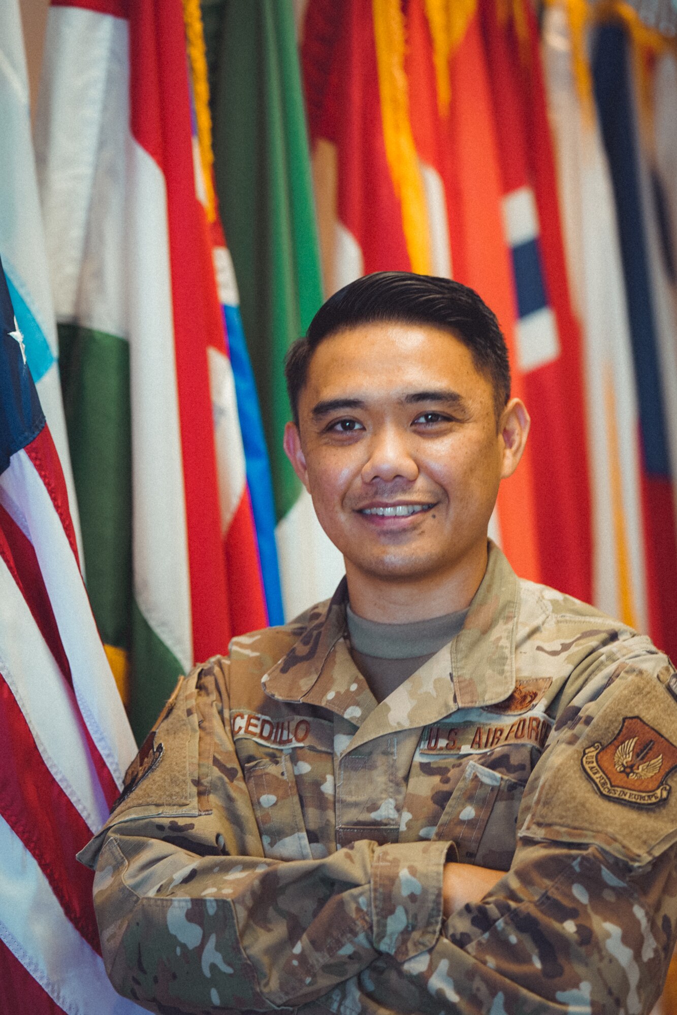 U.S. Air Force Master Sgt. Alexander Cedillo, 52nd Fighter Wing protocol specialist, poses in front of an arrangement of flags at Spangdahlem Air Base, Germany, May, 2020. Cedillo manages high-visibility visits across the 52nd FW and surrounding geographically separated units and advises leadership regarding protocol engagements within the U.S. and international affairs. (Photo courtesy of Master Sgt. Alexander Cedillo)