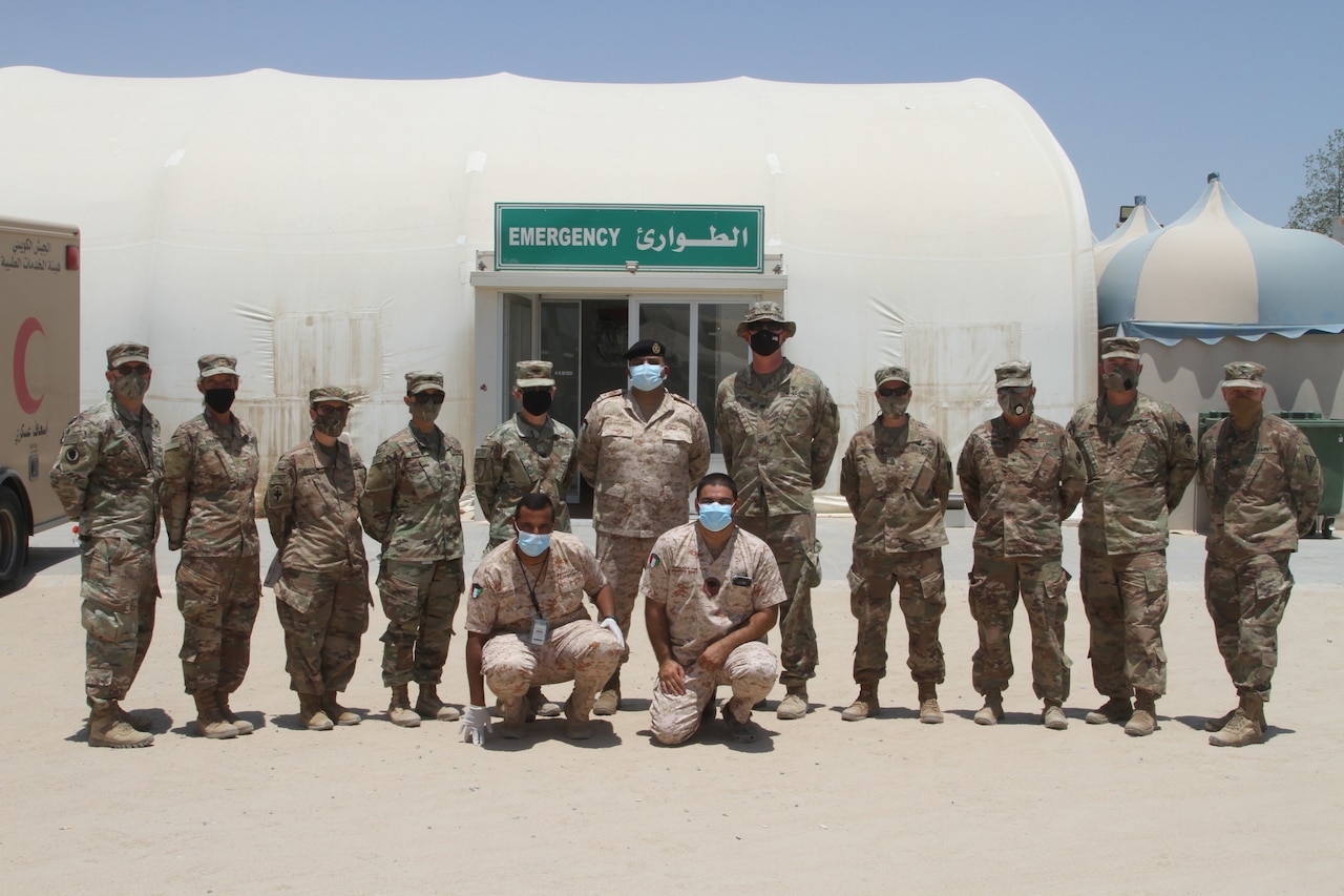 Kuwaiti soldiers pose with U.S. soldiers, all wearing face masks, for a group photo outside a medical tent.