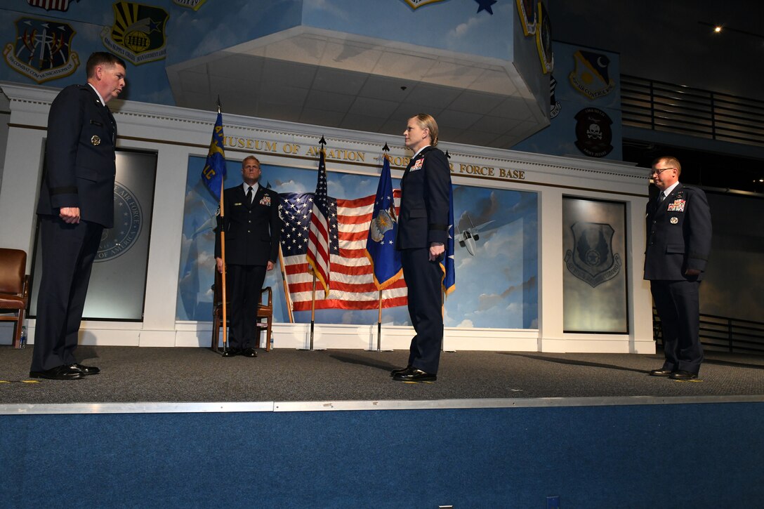 Photos shows four individuals on a stage with one holding the guidon and the other three performing the change of command.