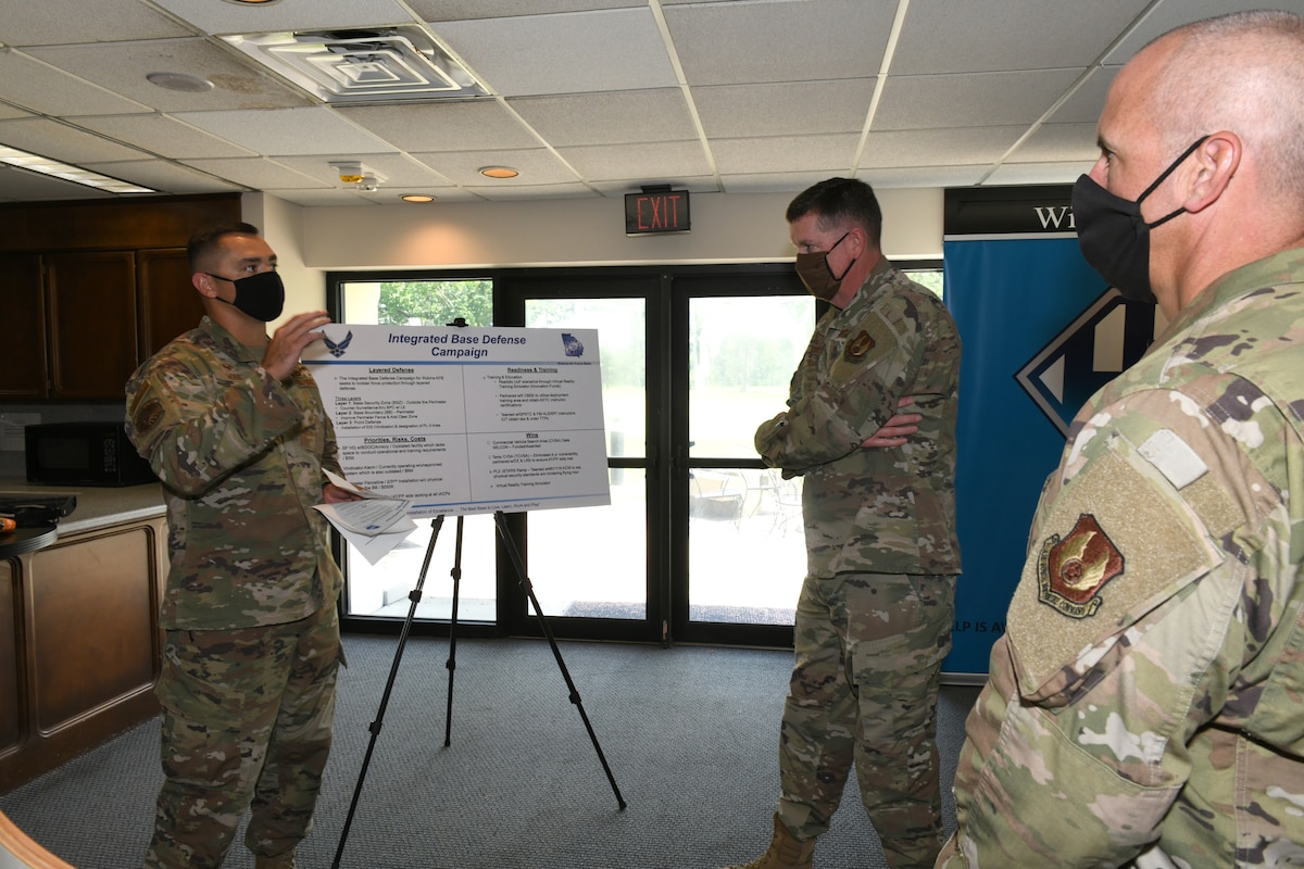 Photo shows three individuals speaking in front of an easel.