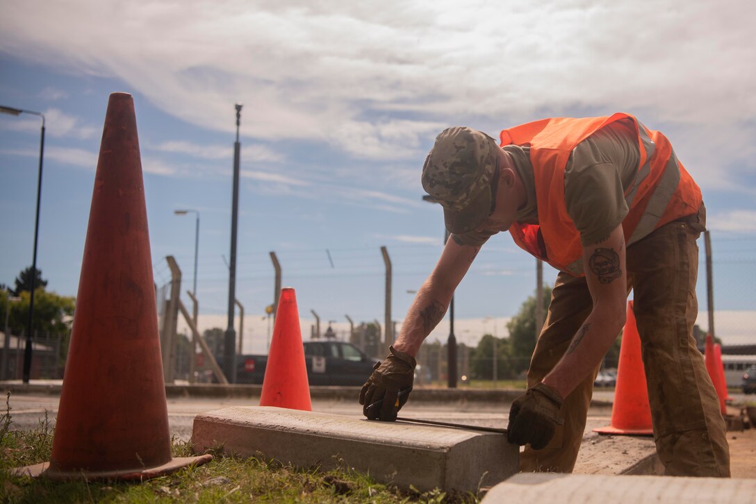 Staff Sgt. Jeffrey Elwell, 100th Civil Engineer Squadron heavy equipment horizontal engineer supervisor, measures a curb at RAF Mildenhall, England, July 12, 2020. The 100th CES Pavements and Construction Equipment Section, whose members are known as Dirt Boyz, removed vehicle barriers and fencing to improve base infrastructure. (U.S. Air Force photo by Airman 1st Class Joseph Barron)