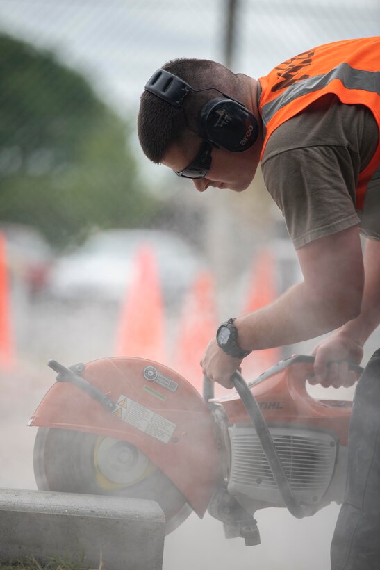 Airman 1st Class Tyler Miller, 100th Civil Engineer Squadron pavement and heavy equipment operator apprentice, cuts through a curb using a K-12 saw at RAF Mildenhall, England, July 12, 2020. Known as “Dirt Boyz,” members of the 100th CES Pavement and Construction Equipment Section removed old vehicle barriers and hedge fencing to upgrade the base’s defense posture. (U.S. Air Force photo by Airman 1st Class Joseph Barron)